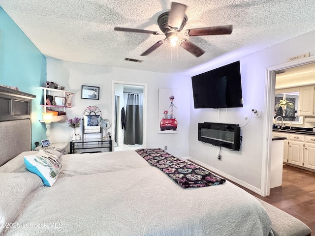5623 87th St, Lubbock, TX 79424 - bedroom with a textured ceiling, wood finished floors, a sink, connected bathroom, and a ceiling fan