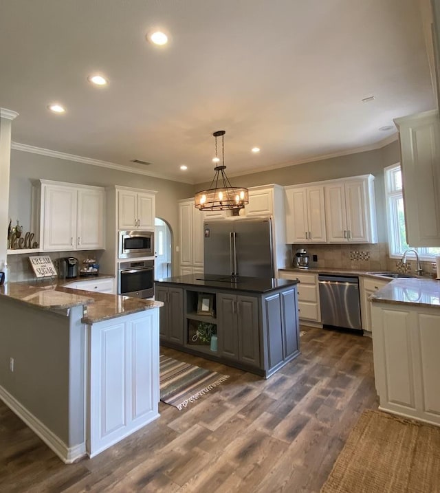 kitchen with decorative light fixtures, white cabinetry, sink, a center island, and built in appliances