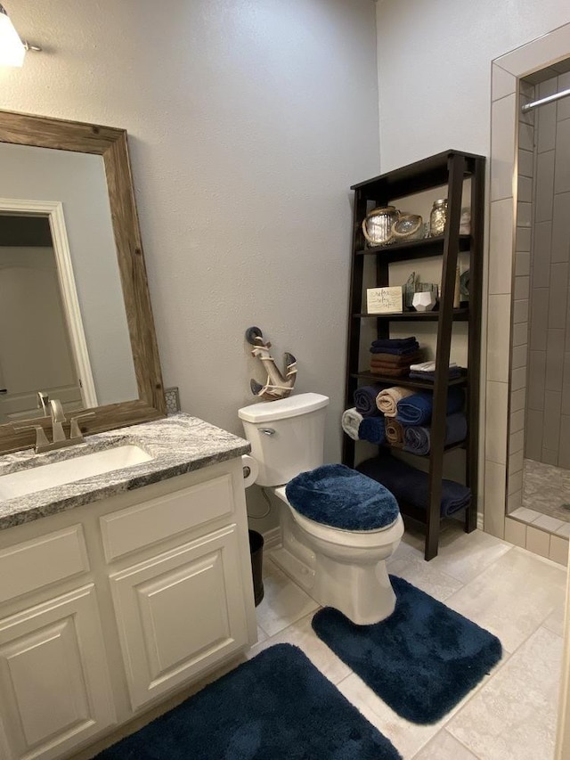 bathroom featuring a tile shower, vanity, tile patterned floors, and toilet