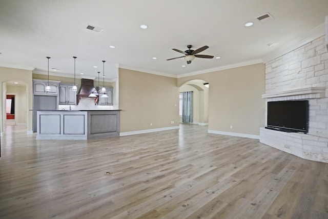 unfurnished living room with crown molding, ceiling fan, a fireplace, and light hardwood / wood-style floors