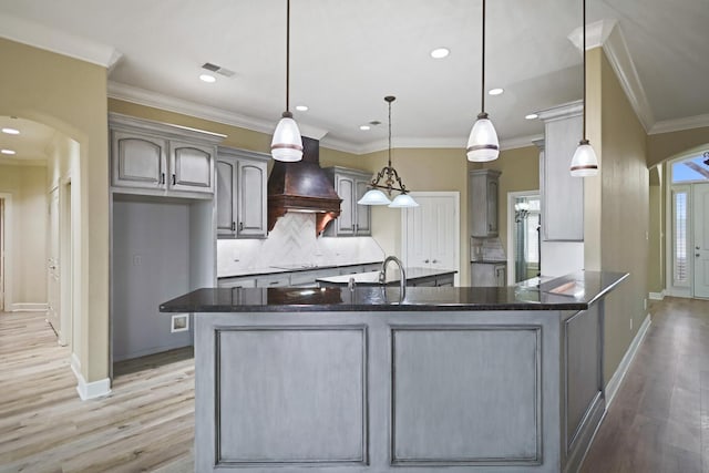 kitchen with decorative light fixtures, backsplash, crown molding, custom range hood, and light hardwood / wood-style flooring