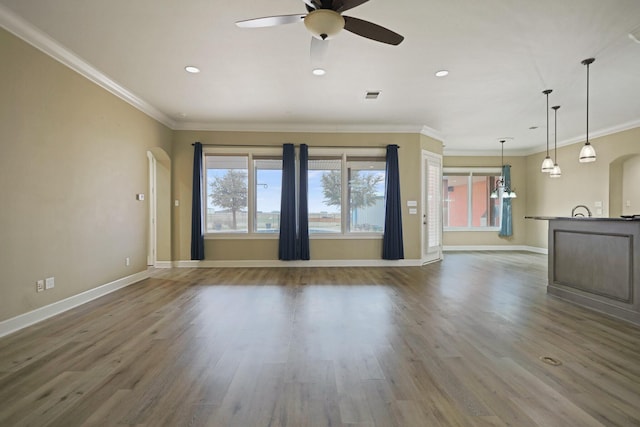 unfurnished living room with wood-type flooring, ornamental molding, and ceiling fan