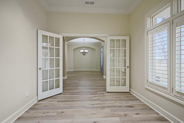 interior space with light hardwood / wood-style floors, crown molding, plenty of natural light, an inviting chandelier, and french doors