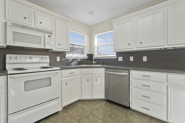 kitchen with white appliances, dark tile patterned flooring, sink, and white cabinets