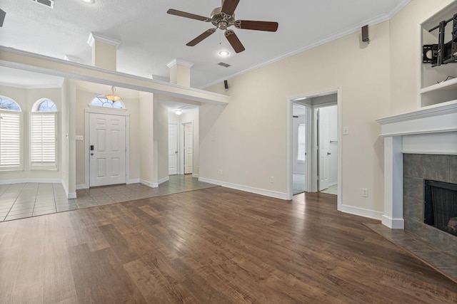 unfurnished living room featuring crown molding, wood-type flooring, a textured ceiling, a tile fireplace, and ceiling fan