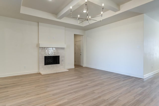 unfurnished living room with beam ceiling, a notable chandelier, a fireplace, and light hardwood / wood-style floors