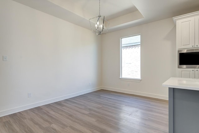 unfurnished dining area with a notable chandelier, light wood-type flooring, and a tray ceiling