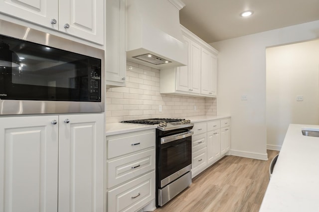 kitchen featuring premium range hood, built in microwave, stainless steel gas stove, light hardwood / wood-style floors, and white cabinets