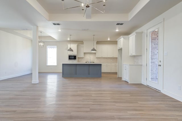 kitchen with pendant lighting, a raised ceiling, a kitchen island with sink, and white cabinets