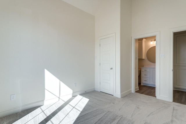 unfurnished bedroom with connected bathroom, a towering ceiling, and light colored carpet