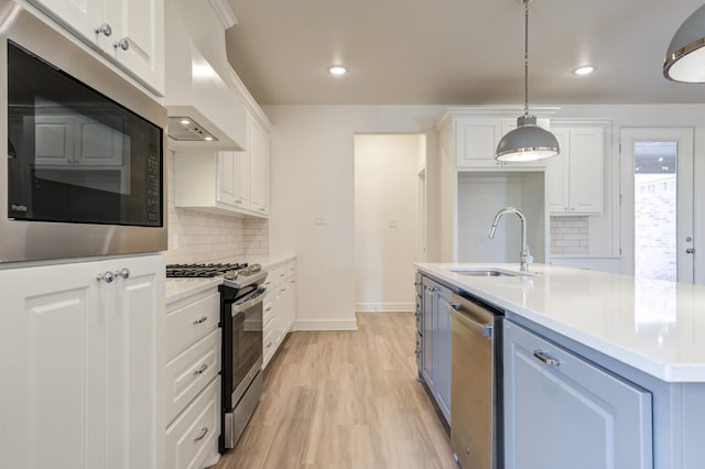 kitchen with sink, white cabinetry, hanging light fixtures, stainless steel appliances, and custom range hood