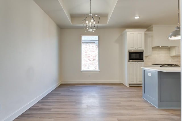 kitchen featuring built in microwave, white cabinetry, decorative light fixtures, and a tray ceiling