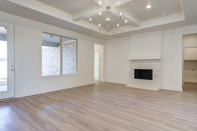 unfurnished living room with a tiled fireplace, beam ceiling, a chandelier, and light hardwood / wood-style floors