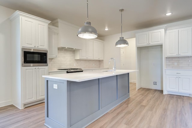 kitchen with built in microwave, white cabinetry, a center island with sink, and pendant lighting