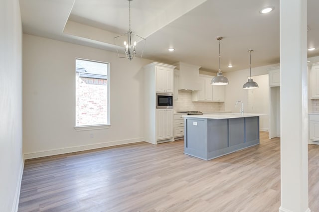 kitchen with white cabinetry, hanging light fixtures, built in microwave, and a center island with sink