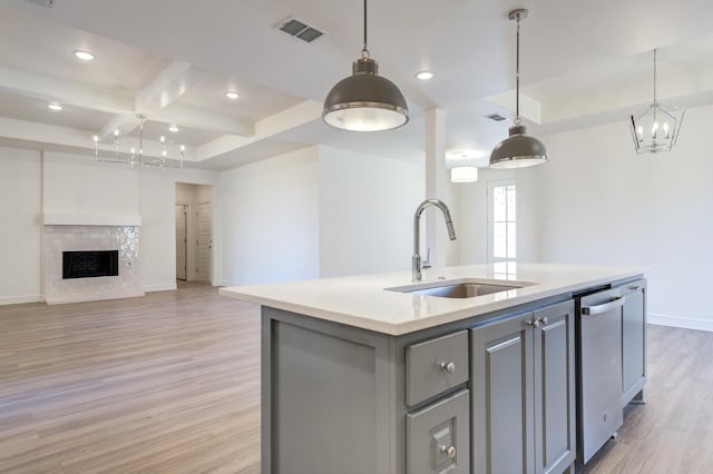 kitchen featuring coffered ceiling, sink, light wood-type flooring, pendant lighting, and a kitchen island with sink