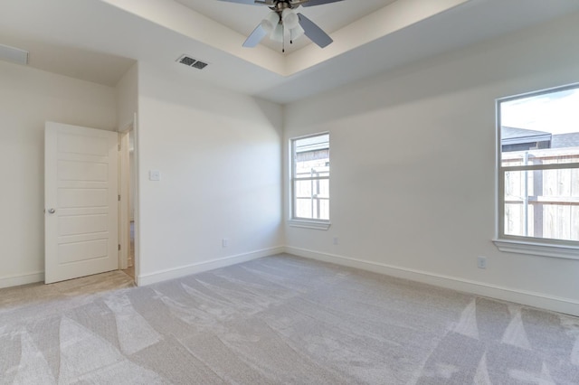 unfurnished room featuring light carpet, a tray ceiling, and ceiling fan