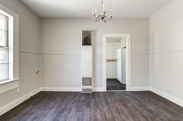 unfurnished room featuring an inviting chandelier and dark wood-type flooring