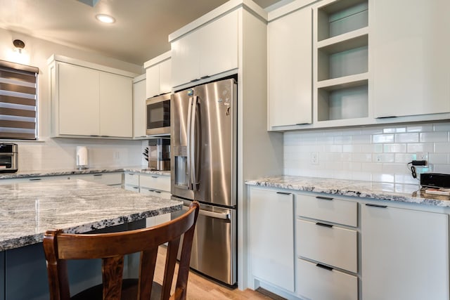 kitchen featuring light stone counters, backsplash, white cabinets, and appliances with stainless steel finishes