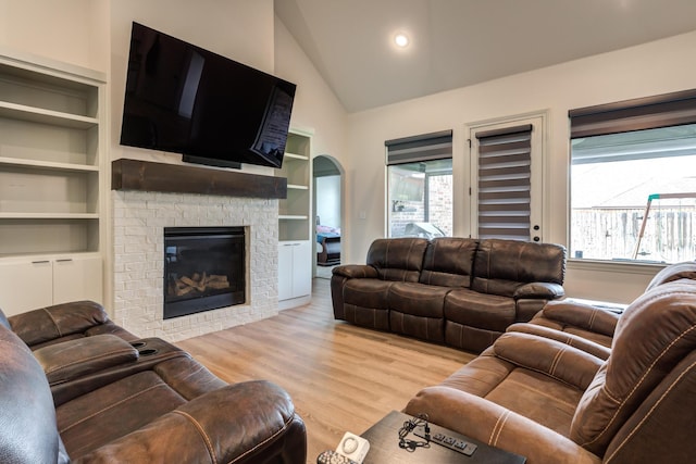 living room featuring lofted ceiling, a fireplace, light hardwood / wood-style flooring, and a wealth of natural light