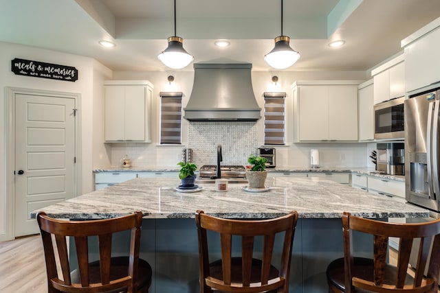 kitchen with extractor fan, appliances with stainless steel finishes, a breakfast bar, white cabinetry, and light stone countertops