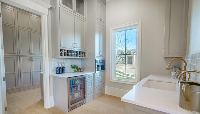 interior space featuring sink, beverage cooler, backsplash, and light hardwood / wood-style flooring