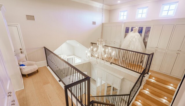 stairway with hardwood / wood-style floors, ornamental molding, and a chandelier