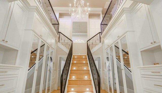 staircase featuring a notable chandelier, crown molding, hardwood / wood-style floors, and a high ceiling