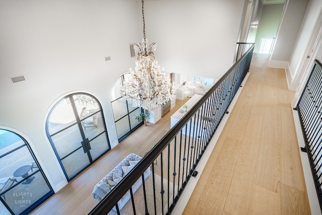 hallway with an inviting chandelier, a towering ceiling, and light hardwood / wood-style floors