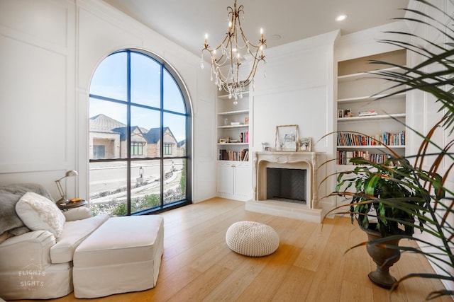 living area with an inviting chandelier, light wood-type flooring, and built in shelves