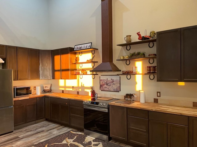 kitchen with wood counters, island range hood, dark brown cabinets, stainless steel appliances, and light hardwood / wood-style floors