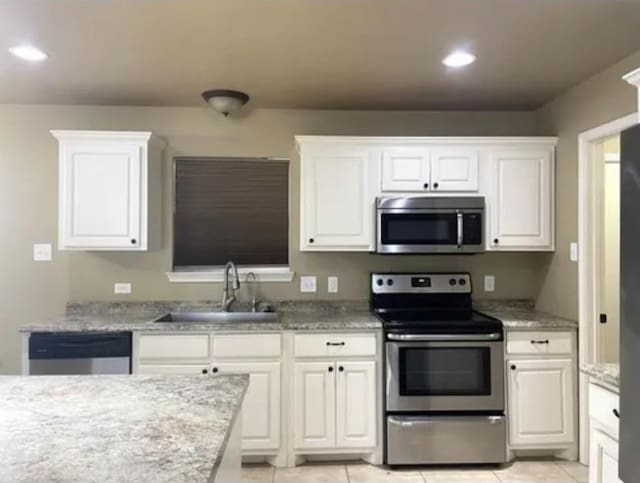 kitchen featuring sink, light tile patterned floors, white cabinetry, stainless steel appliances, and light stone counters