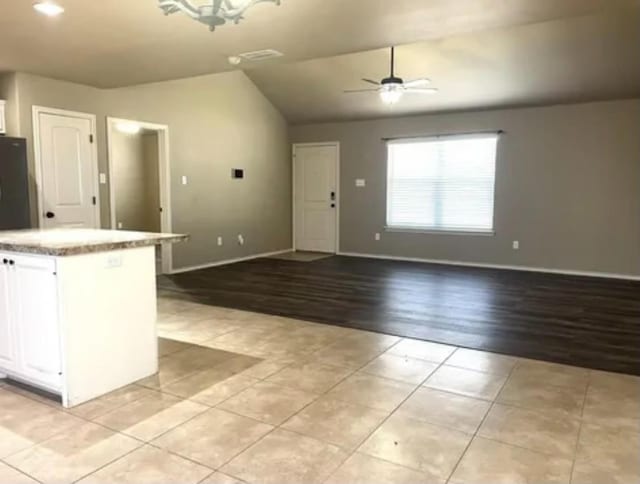 kitchen featuring light tile patterned flooring, white cabinetry, a center island, vaulted ceiling, and ceiling fan