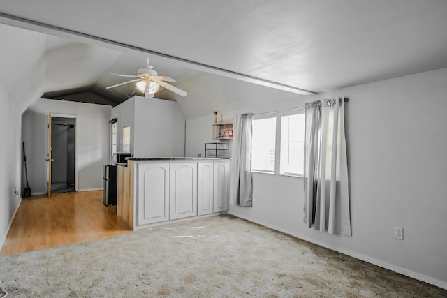 kitchen with baseboards, ceiling fan, dark countertops, vaulted ceiling, and light colored carpet