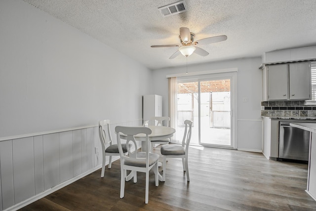 dining room with visible vents, ceiling fan, a textured ceiling, wood finished floors, and a wainscoted wall