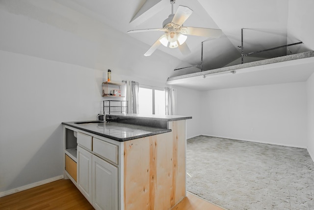 kitchen featuring baseboards, a peninsula, dark countertops, lofted ceiling, and a sink