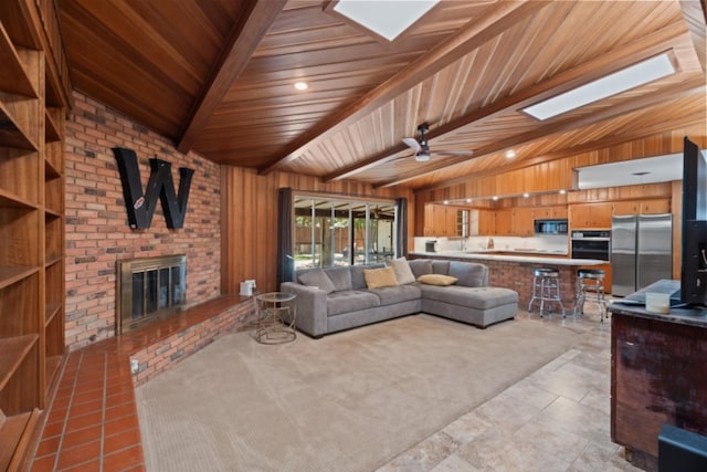 living room featuring light tile patterned floors, ceiling fan, wooden walls, vaulted ceiling with skylight, and a fireplace