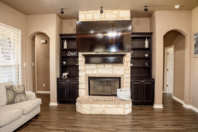 unfurnished living room featuring a stone fireplace, dark hardwood / wood-style floors, and built in shelves