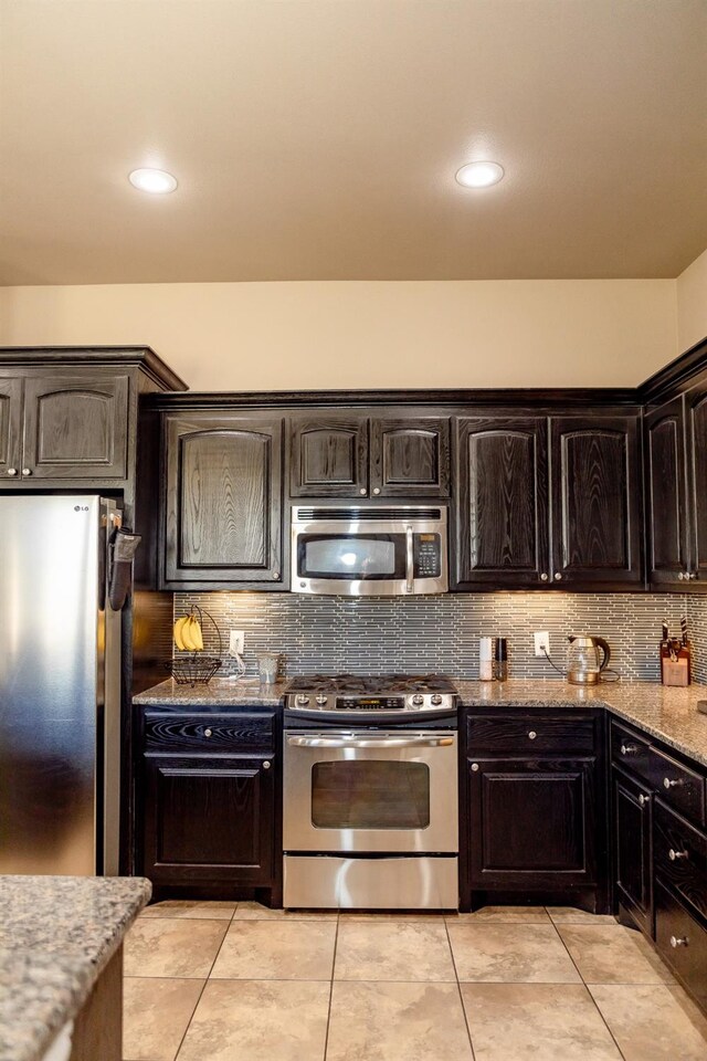 kitchen featuring appliances with stainless steel finishes, backsplash, light tile patterned floors, dark brown cabinetry, and light stone counters