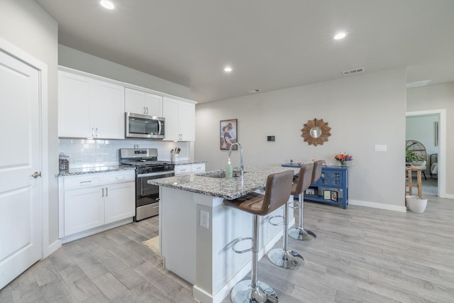 kitchen featuring white cabinetry, appliances with stainless steel finishes, light stone counters, and a center island with sink