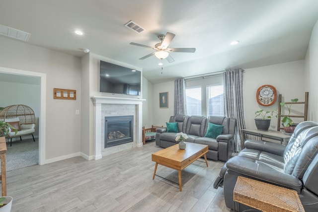 living room with a tiled fireplace, ceiling fan, and light wood-type flooring