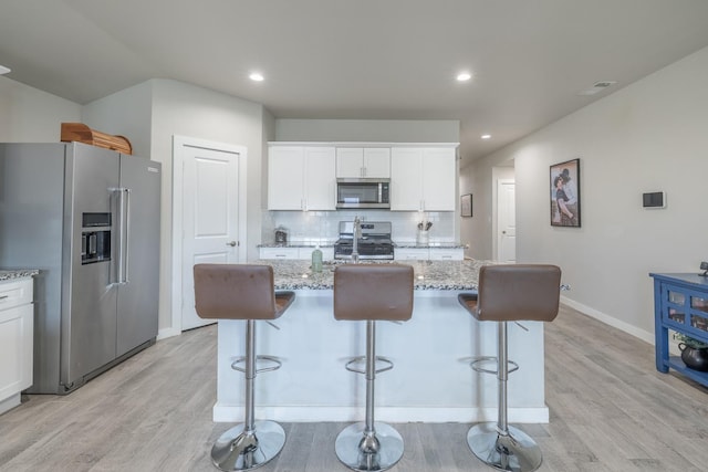 kitchen featuring appliances with stainless steel finishes, tasteful backsplash, light stone countertops, white cabinets, and a center island with sink