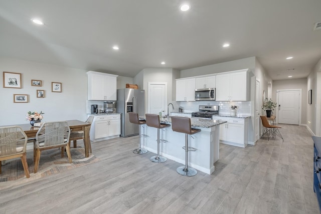 kitchen featuring a kitchen island with sink, light stone countertops, white cabinetry, and stainless steel appliances