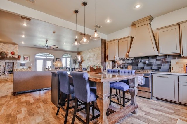 kitchen featuring premium range hood, decorative light fixtures, backsplash, light hardwood / wood-style floors, and gas stove