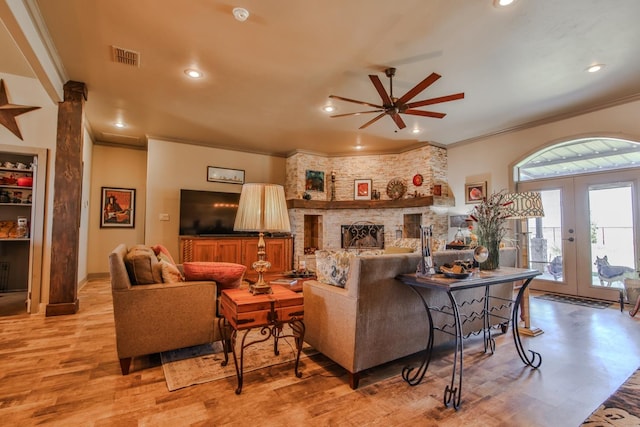 living room with french doors, a large fireplace, ceiling fan, crown molding, and light hardwood / wood-style flooring