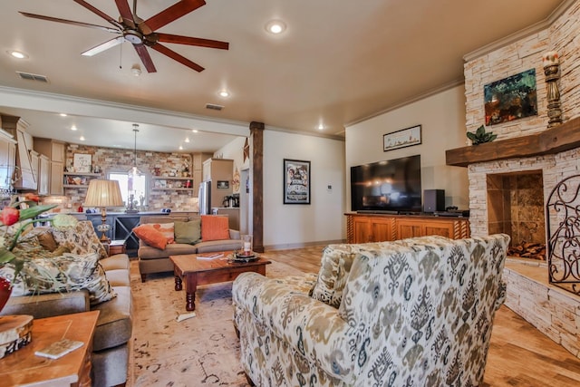 living room with ornamental molding, a stone fireplace, ceiling fan, and light hardwood / wood-style flooring