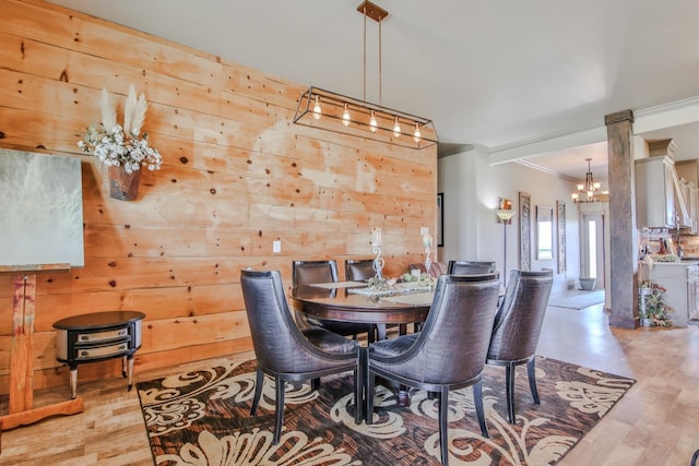 dining room featuring wooden walls, decorative columns, ornamental molding, a chandelier, and light wood-type flooring