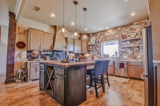 kitchen with appliances with stainless steel finishes, hanging light fixtures, a kitchen breakfast bar, a center island, and wood counters