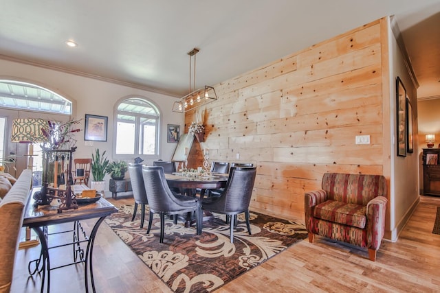 dining area with crown molding, wooden walls, and light hardwood / wood-style floors