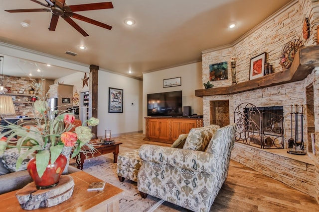 living room with crown molding, ceiling fan, a stone fireplace, and light wood-type flooring